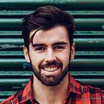 A man with beard and red plaid shirt smiling.